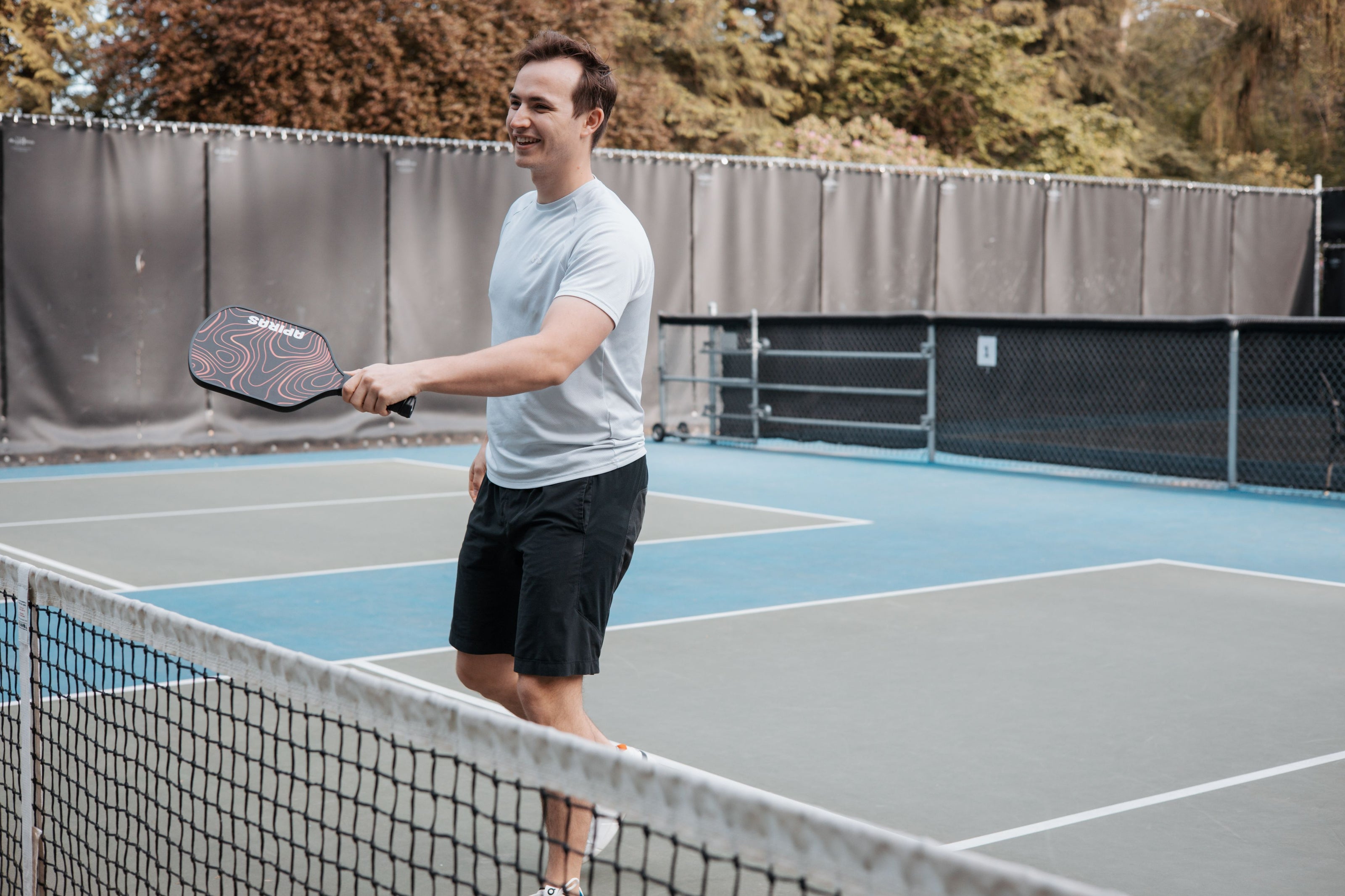 Man on a pickleball court smiling while holding a pickleball paddles